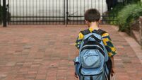 Boy with backpack holding bag walking toward closed hate