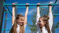 Two girls hang on the horizontal bar on the playground.