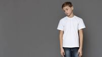 Sad teen boy standing alone, grey studio background