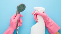Woman hands in protective rubber gloves holding white plastic spray bottle and shower head on light blue table background. Paste
