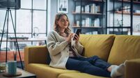 Beautiful Caucasian Female Using Smartphone in Stylish Living Room while Resting on a Cozy Couch Sofa. Young Woman at Home, Brow