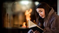 Young girl reading a book by the fireplace