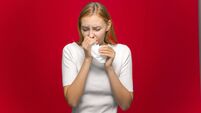 Sick girl suffer chill, flu. influenza symptom or allergy covering runny nose with handkerchief on red studio background