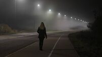 Young woman alone slowly walking under white street lights in night. Dark time. Peaceful atmosphere in mist. Foggy air. Back vie
